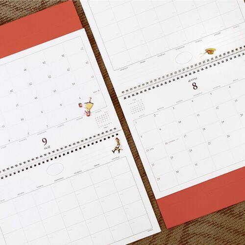Close-up pages reveal generous daily boxes, fine grid lines, and small decorative artwork around the monthly layout.