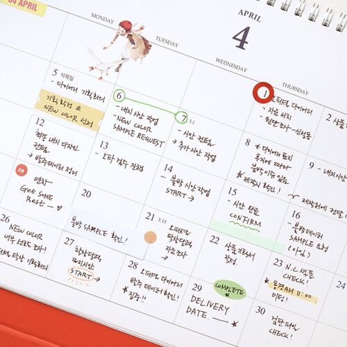 A hand holds the April page above the red base, showing the broad landscape format and clearly separated daily boxes.