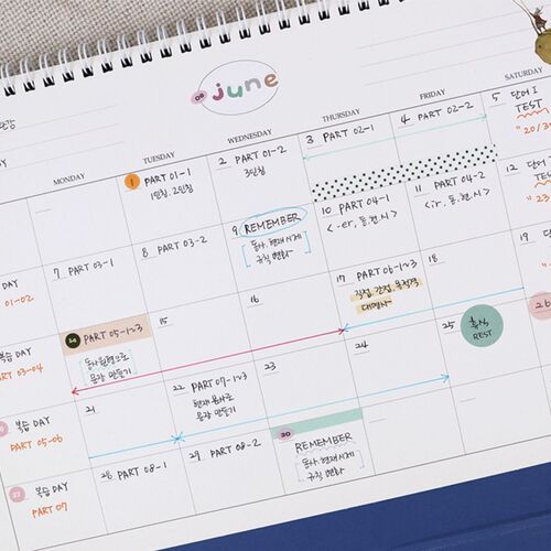 A hand writes on a dated page while the blue base keeps the large scheduler steady on the desk.