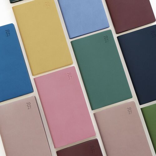 Several cover colors lean together on a glass shelf while an open scheduler rests nearby with a monthly grid visible.