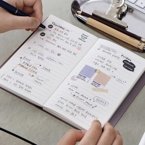 A monthly page is written with colorful markers and reminders beside a laptop and desk accessories.
