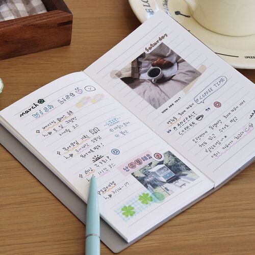 The scheduler is held open over a laptop, showing its broad writing surface and practical workday setting.