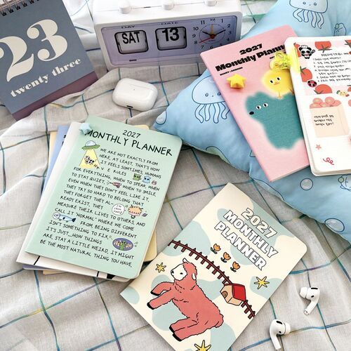 Several planners rest among everyday desk and travel items, showing how the slim format fits naturally into daily routines.