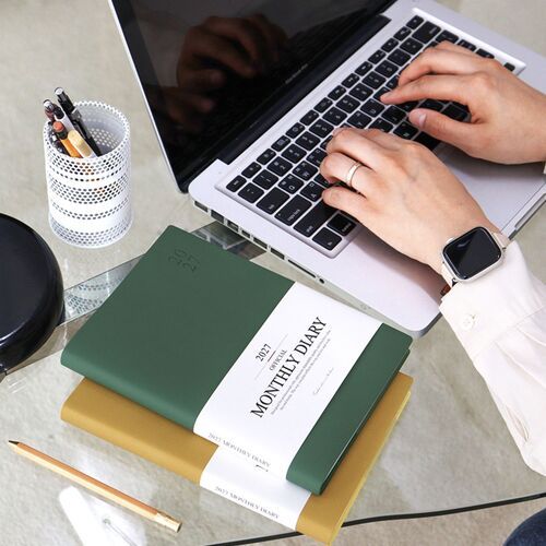 A Green Mousse scheduler is held open in both hands, highlighting its slim rectangular format.