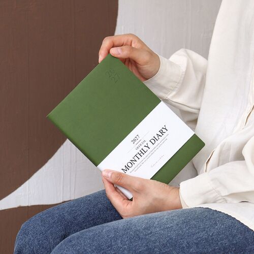 A Mocha Mousse scheduler lies over reading material, creating a calm desk or lounge setting for planning.