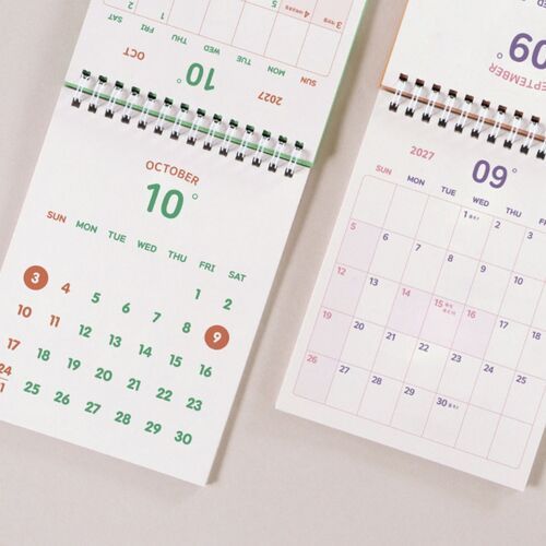 Photo 15: A Smile Green calendar stands open on an October monthly grid beside a small clock and desk accessories.