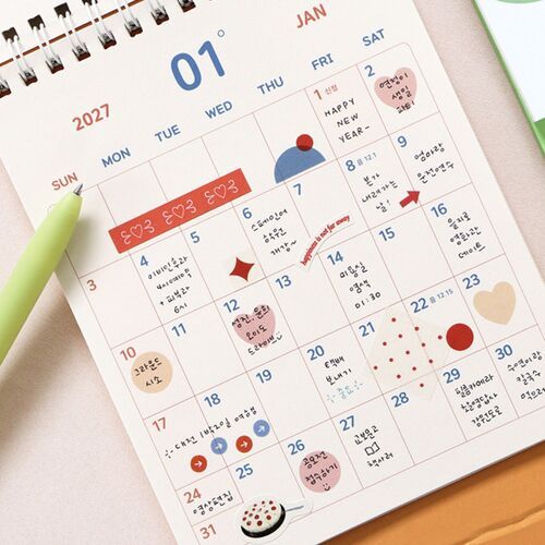 Photo 13: A Smile Green calendar sits beside loose planning pages and a blue pencil, with its smile-face cover centered in view.