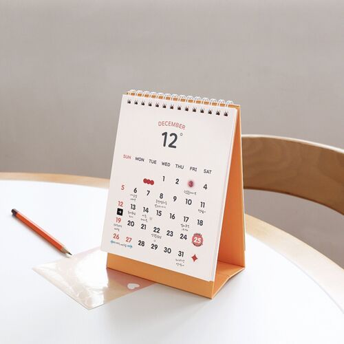 Photo 20: The spiral-bound calendar stands on a white shelf, where its green base and smile-face cover add a bright accent.