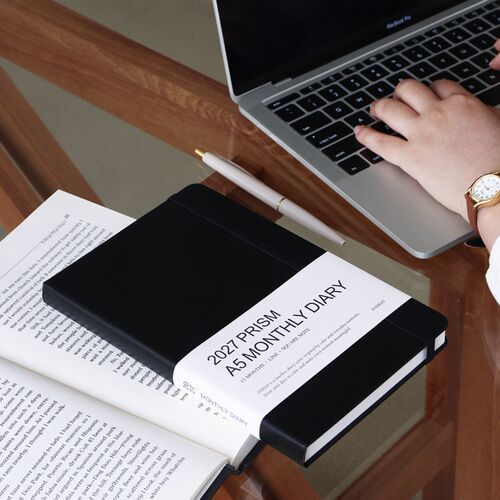 The planner is placed on a desk beside a laptop and paper clip, with the Sunset Purple cover prominently visible.