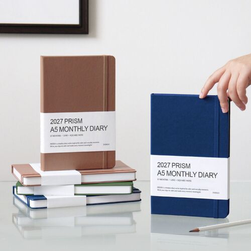 A Classic Blue planner leans against books while a second blue cover sits behind it, showing the textured finish.