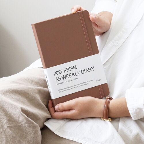 Mocha Mousse is shown in hand with its matching elastic band and white bellyband wrapped around the hardcover.