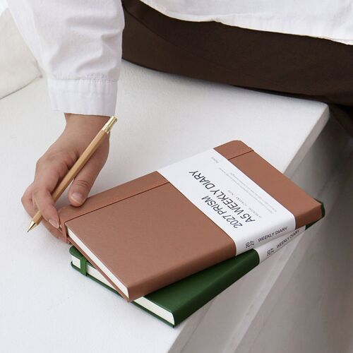 A blue planner is held open near a doorway, showing its flexible everyday use beyond the desk.