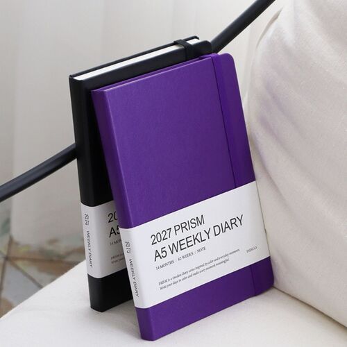 A purple planner stands beside a laptop and pen, presenting a simple workspace arrangement.