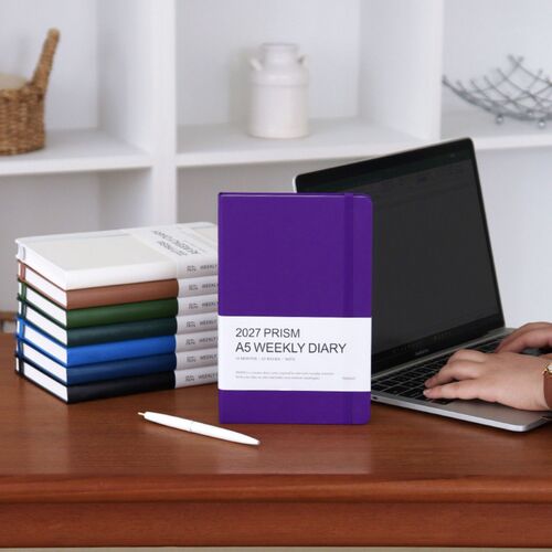 A Mocha Mousse planner lies over a Forest planner, showing the hardcover edges and matching elastic closures.