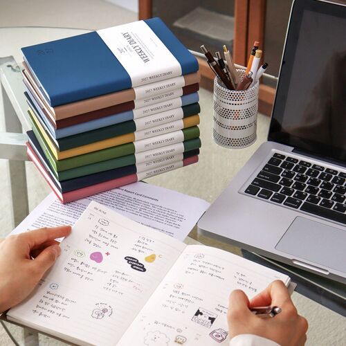 Navy and other scheduler colors sit beside a laptop and stationery, presenting a practical desk-planning setup.