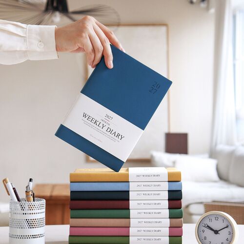 Green Mousse rests on folded fabric with its white weekly diary band still wrapped around the cover.