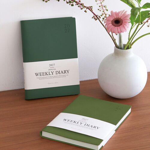 A hand holds the open scheduler while the printed weekly diary title band remains visible across the cover.