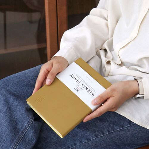 A tan Mustard scheduler rests across someone’s lap with the white title band facing upward.