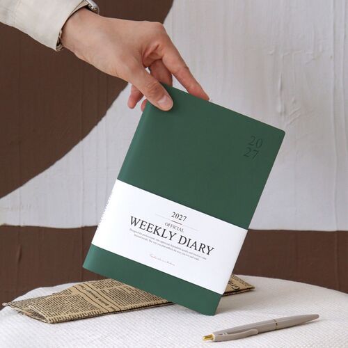 A hand opens the Mustard scheduler, showing the cover, title band, and thick page block.
