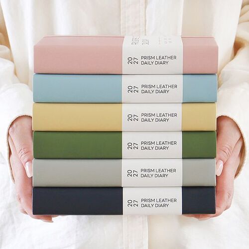 Six closed B6 planners are stacked together, showing the Rose Mellow, Water Mellow, Butter Mellow, Green Mellow, Stone Mellow, and Ink Mellow covers.
