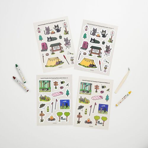 A hand uses tweezers to place a cat camping sticker on a white surface, showing the individual decorative pieces in use.