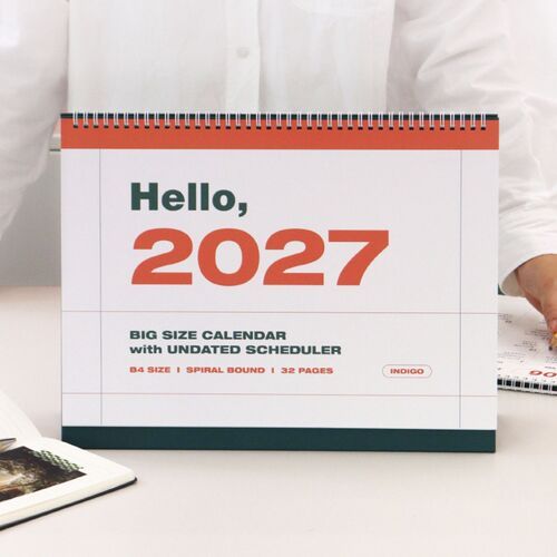 The cover displays bold coral and dark green 2027 lettering above the spiral-bound B4 calendar and deep green tabletop stand.