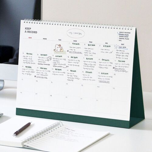 A clean desktop scene shows the coral-and-green cover positioned near a monitor and active planning materials.