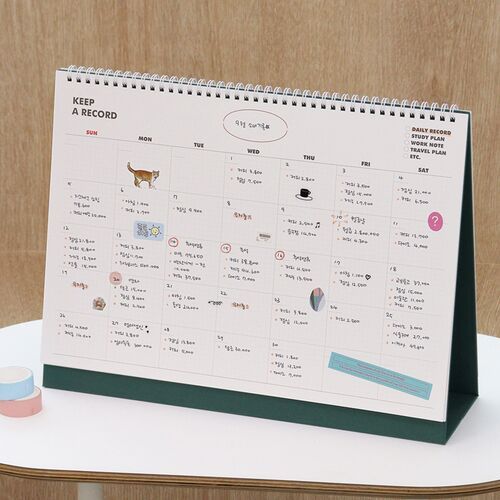 A hand writes in the open calendar while the cover remains visible behind it, emphasizing its use during daily planning.