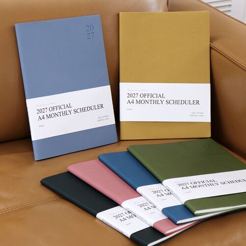 Powder Blue and Mustard schedulers stand against a sofa, showing the clean cover design and wide A4 proportions.