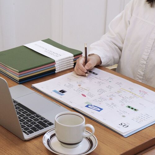 The Powder Blue scheduler is displayed in hand beside stacked color options, emphasizing its light cover and A4 size.