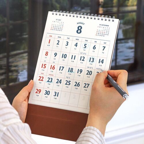 A close view shows the white spiral binding and large monthly layout while the calendar is held for writing.