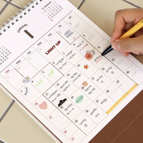 A hand writes into a January grid, demonstrating the usable writing space within each monthly date box.