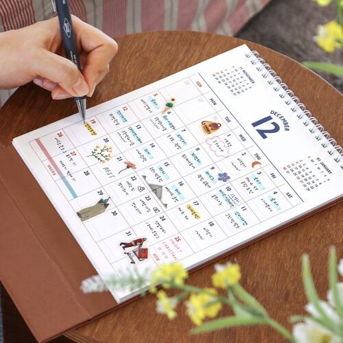 The calendar sits near a coffee cup and desk items, presenting a relaxed planning setup for daily routines.