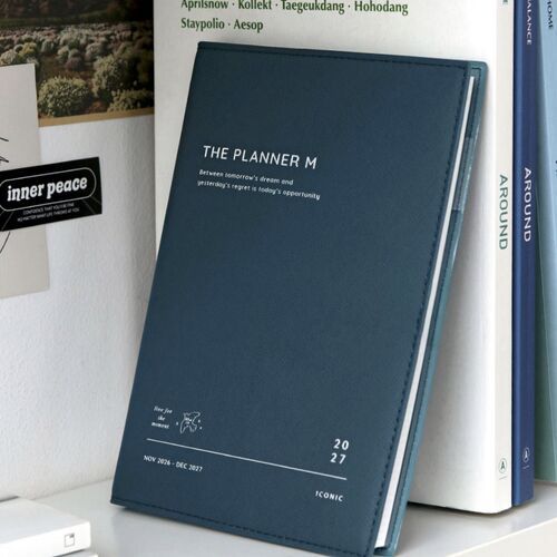 Steel Blue stands against books, highlighting its deep cover color, stitched border, and understated printed lettering.