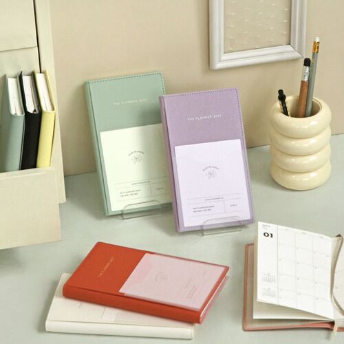 Several planner colors are arranged on a desk, showing the slim format alongside books, stationery, and a small pencil cup.