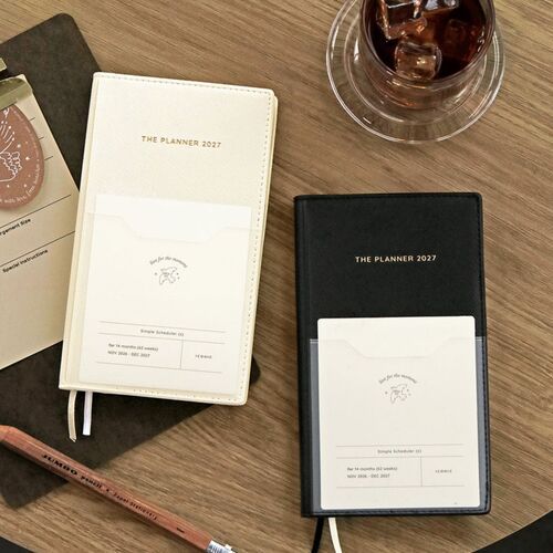 Milk White and Black planners lie on a wooden tabletop, each showing the front pocket and centered title.
