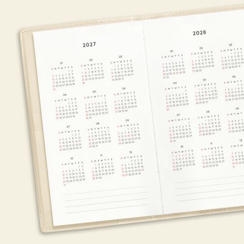 Two ribbon bookmarks fall from an open weekly spread, while a pen rests in the planner’s side loop area.