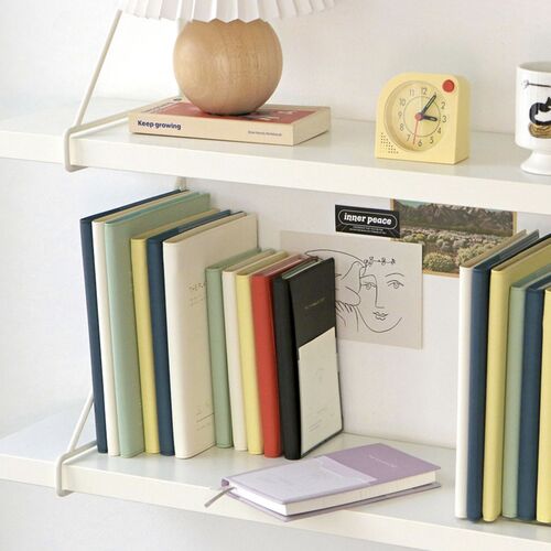 Several planners are stacked on a pink surface, with the Vermilion cover and front pocket visible at the top.