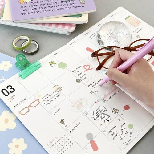 An open monthly spread shows roomy date boxes with decorative illustrations and space for handwritten plans.