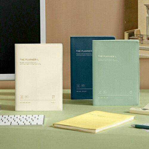 The Planner L appears in Cream, Deep Teal, and Mint, with a fourth Lemon Yellow cover resting on the desk.