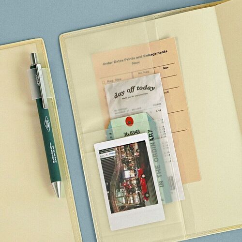 An open planner displays transparent cover pockets holding cards and paper pieces beside a pen.