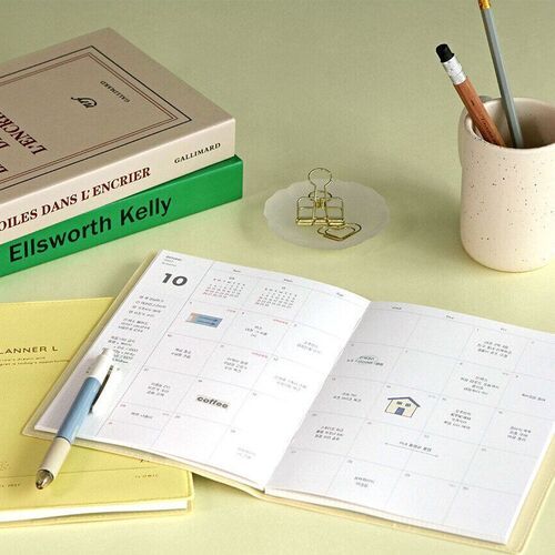 An open monthly spread demonstrates the flat-opening format, with a pen resting beside the dated grid.