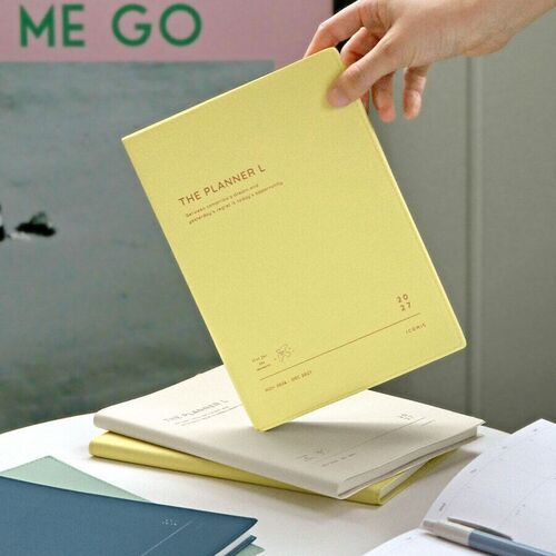Mint and Cream planners rest together on a blue surface, showing their textured covers and understated printed designs.