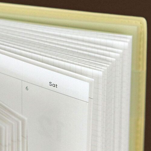 Lemon Yellow is held upright above stacked planners, giving a clear view of its cover, rounded corners, and slim binding.