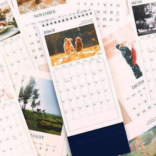 Loose monthly pages surround the calendar on a tabletop, showing the variety of seasonal photographs and clean date layouts.