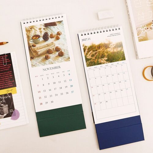 Two calendar pages are mounted on a wall above the desk calendar, showing different monthly photographs and the upright base below.