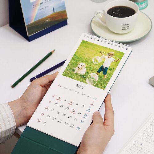 The calendar stands beside a vase and dishware, showing its decorative photo cover and stable triangular silhouette.