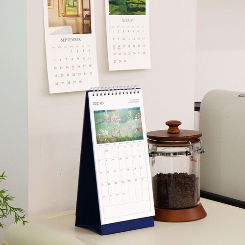 An open monthly page reveals a bright ocean image above a spacious grid, with the standing base supporting it behind.