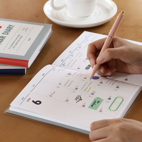 The planner is open beside a cup and pen, presenting a monthly calendar page ready for handwritten entries.