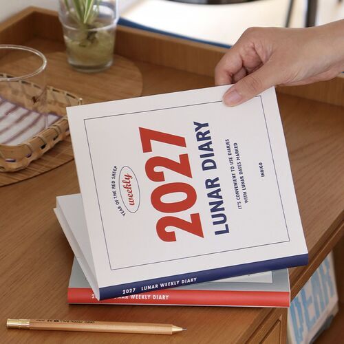A hand lifts the planner to show the Red and Navy cover options and slim bound profile.